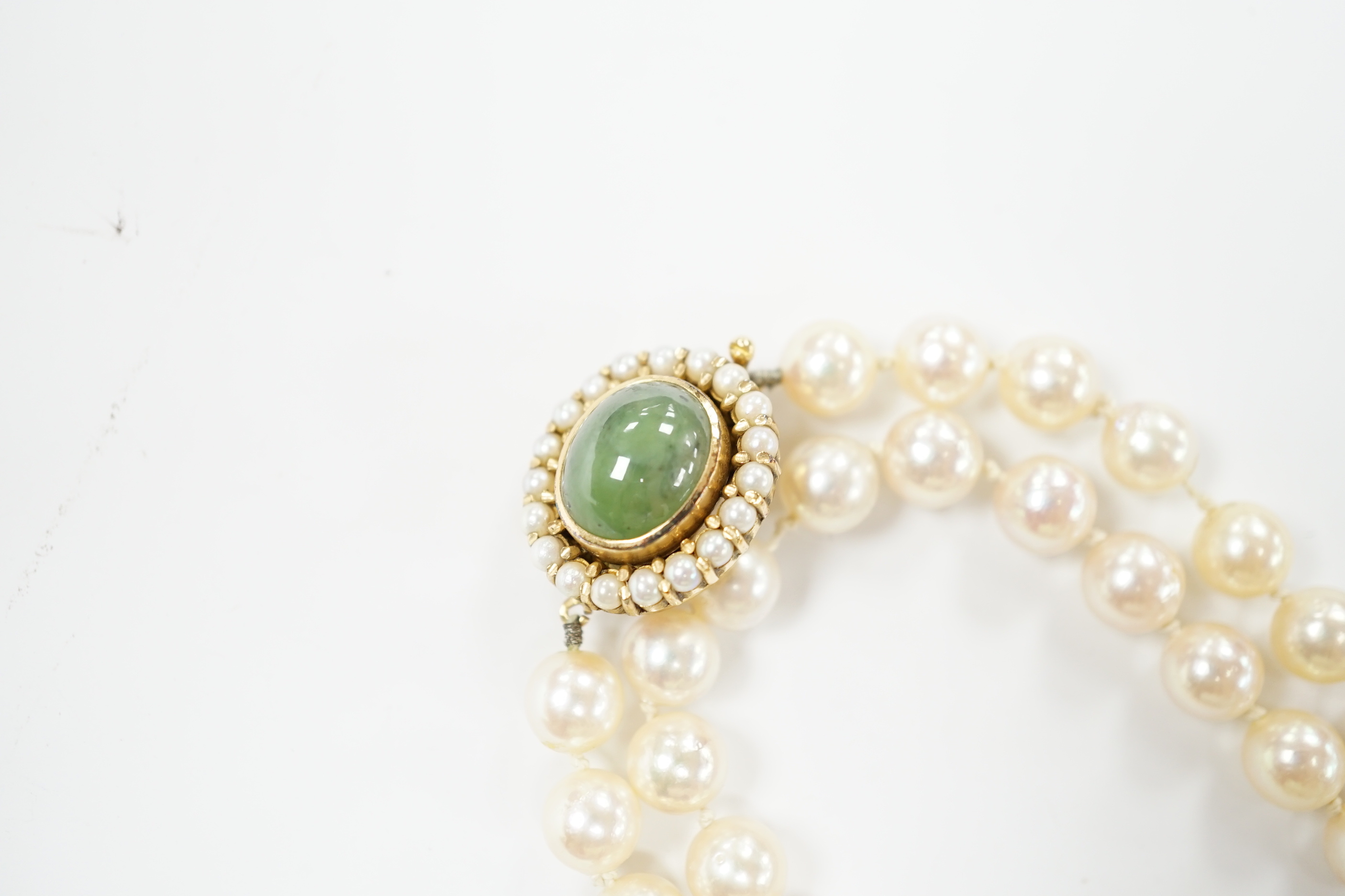 A Portuguese single strand cultured pearl necklace, with cabochon nephrite and seed pearl cluster set yellow metal clasp, 86cm.